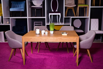 Shop, sale of furniture in a shopping center. Exposition sample Dining wooden table with textile chairs in gray on a white shelf with furniture and a pink carpet