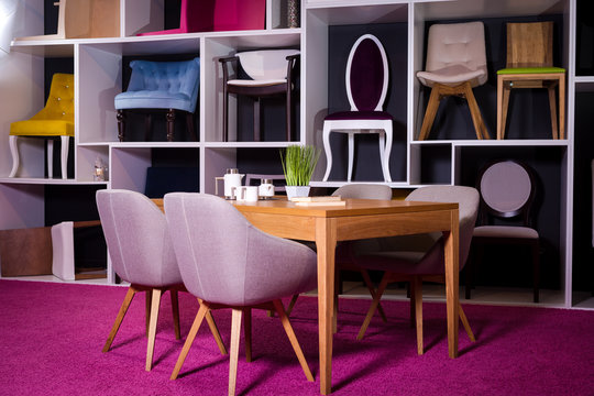 Shop, sale of furniture in a shopping center. Exposition sample Dining wooden table with textile chairs in gray on a white shelf with furniture and a pink carpet