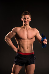 Fototapeta na wymiar Man athlete with sport bottle on dark background