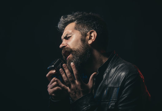 Life style concept - handsome man with beard wearing black leather jacket holding microphone and singing. Emotional portrait attractive singer with beard and mustache. Bearded man singing karaoke.