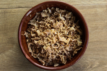 Stone bowl with fried onions on wooden background