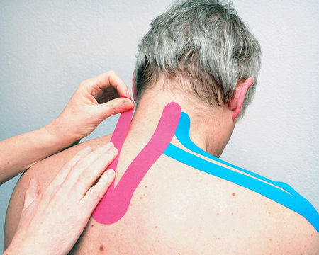 female physiotherapist applies tape on back of older grey haired caucasian man