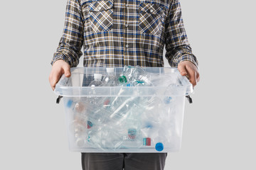partial view of man holding container with plastic bottles in hands isolated on grey, recycling concept