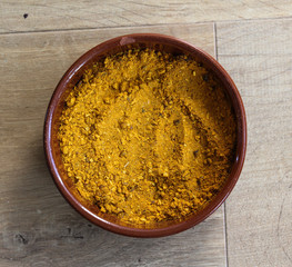 Stone bowl with yellow turmeric curry powder on wooden background