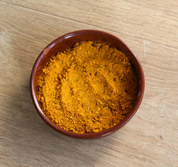 Stone bowl with yellow turmeric curry powder on wooden background