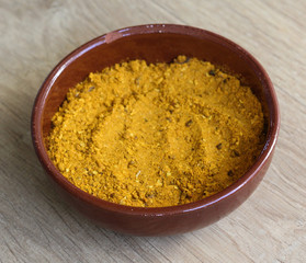 Stone bowl with yellow turmeric curry powder on wooden background