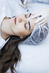 Beautician female applies permanent makeup on eyebrows, tattoo eyebrows on beautiful models in a...