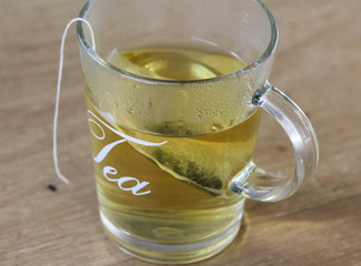 Glass of jasmin tea with tea bag on wooden background