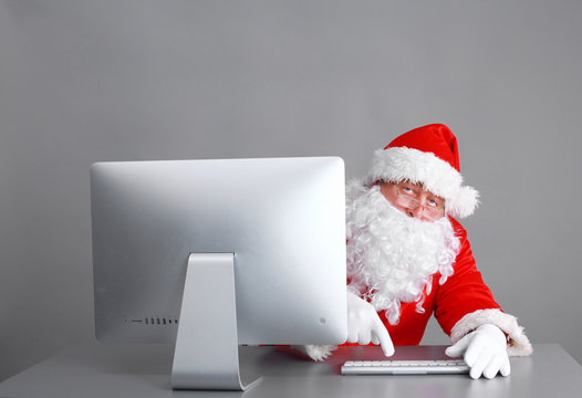 Santa Claus reading children letters and writing responses to them using laptop