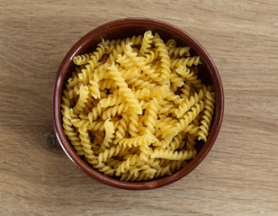 Stone bowl with italian raw uncooked fusilli pasta on wooden background