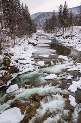 Winter landscape. Mountain river flows from the rocks. Snow and mountain river