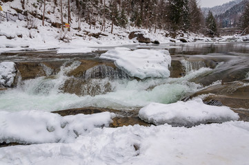 Winter landscape. Mountain river flows from the rocks. Snow and mountain river