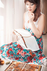 Young beautiful woman is engaged in embroidering a dagger on the embroidery frame in a colored...