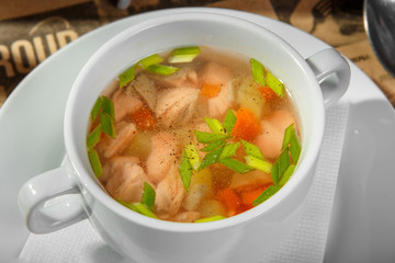 Transparent soup with chicken, fish carrots and herbs, black ground pepper, in a deep white plate. Filing for a restaurant, bar, cafe. Light, low-calorie dinner. Close up