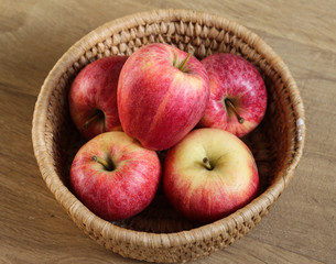 Fresh red and yellow royal gala apples in straw basket on wooden background