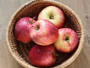 Fresh red and yellow royal gala apples in straw basket on wooden background