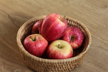 Fresh red and yellow royal gala apples in straw basket on wooden background