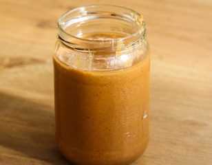 Glass jar pot with homemade peanut butter on wooden background