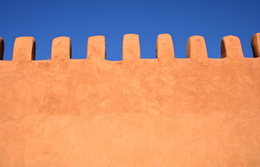 Pięknie wykończony zabytkowy mur w kolorze brzoskwiniowym w stylu arabskim, w tle piękny błękit nieba - obrazy, fototapety, plakaty