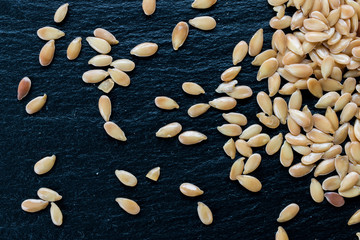 Golden flax seeds on black slate background, macro, top view