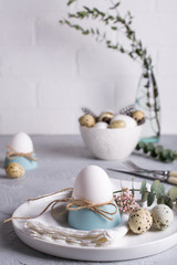 Easter  festive table setting with white chicken  eggs in eggs cups, leaf sprigs of eucalyptus. On a gray concrete background.