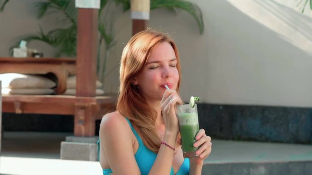 Young caucasian woman drinking green juice in blue swimsuit