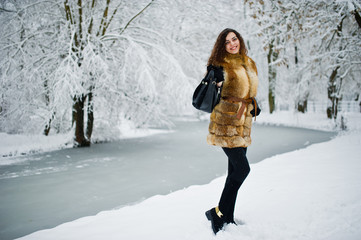 Fototapeta na wymiar Elegance curly girl in fur coat at snowy forest park at winter.