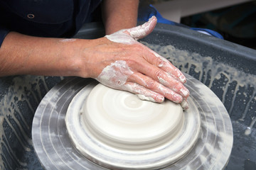 A lady ceramics artist at work in her home pottery studio, throwing a bowl on a wheel. Opening up.