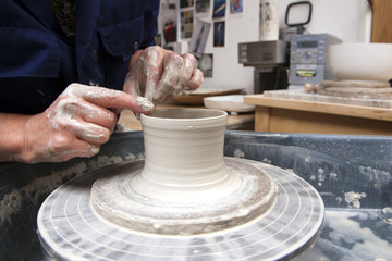 A lady ceramics artist at work in her home pottery studio, forming a mug shape