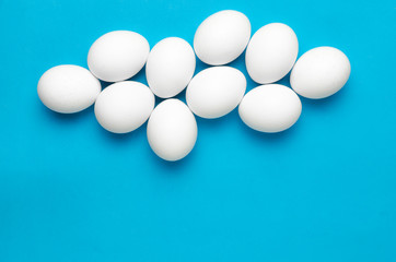 White chicken eggs the shape of clouds on bright blue background.