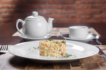 Serving salad in a cafe, restaurant on a white plate with cutlery. Laying, background brick wall, in a low key, a teapot and a cup of tea. The beginning of a meal, lunch