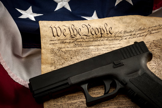 The second amendment and gun control in america concept with a handgun and the american constitution on the USA flag with close up on the "we the people" part of the united states constitution