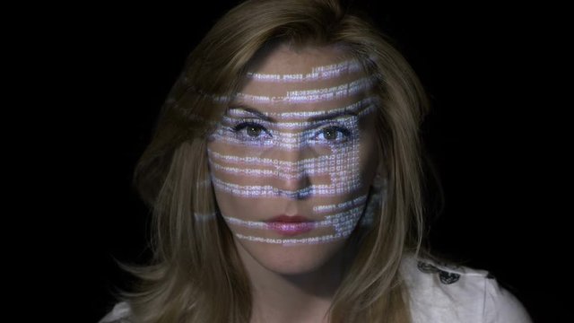 Portrait of a young blonde woman computer programmer coding while binary data characters are projected on her face