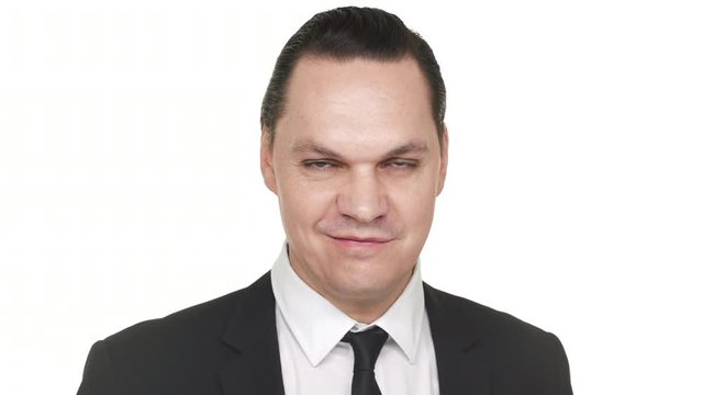 Horizontal closeup portrait of serious man 30s in black business suit grinning and behaving sarcastically, over white background in studio. Concept of emotions