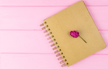 A sketchbook on a pink wooden background with a dry rose.