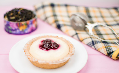 Tartlet with berries and cream on a white plate on a pink wooden background.