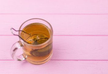 Tea in a glass with a teapot-spoon on a pink wooden background.