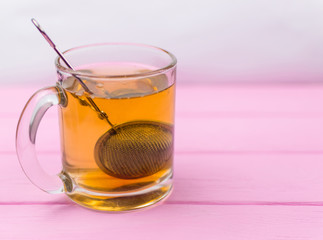 Tea in a glass with a teapot-spoon on a pink wooden background.