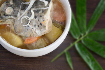 Japanese soup (Miso) with head salmon and vegetables in white bowl on brown wooden table, Decoration with bamboo leaf.