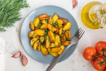 Fried potatoes in a plate. Baby potatoes, green, tomatoes and garlic on the table