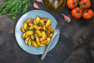 Fried baby potatoes, green, tomatoes and garlic on a dark background