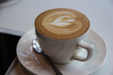 In selective of heart picture from cream foam of cuppuccino coffee cup put on table and coffee shop,blurry light around.