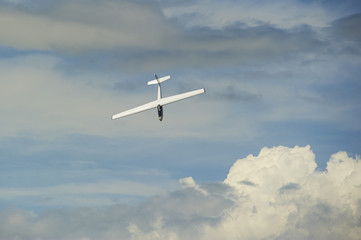 A Glider flying in blue sky with big white clouds. The glider is a plane that has no engine
