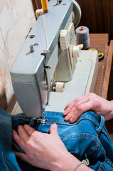 hands of an elderly seamstress working with jeans on a sewing machine