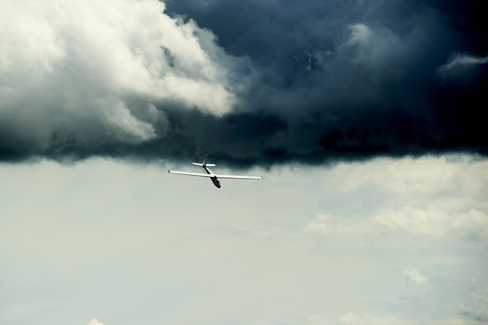 A Glider flying away from storm. The glider is a plane that has no engine.
