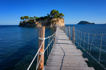 Fototapeta premium Widok z wyspy Agios Sostis i Cameo. Piękna mała wyspa z drewnianym mostem i turkusową wodą. Zakynthos Grecja.