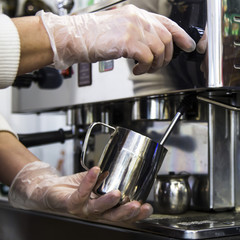 Fototapeta na wymiar A barista at a cafe churns milk in a metal jug using a caper of professional coffee machine. Coffee house concept. The process of making cappuccino or latte
