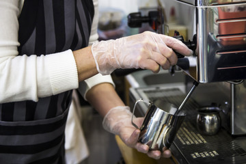 A barista at a cafe churns milk in a metal jug using a caper of professional coffee machine. Coffee house concept. The process of making cappuccino or latte