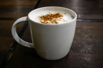Fotobehang Hot coffee cappuccino mug with cinnamon powder sprinkle on top milk foam on dark wood table blurred background, close up. © Chansom Pantip