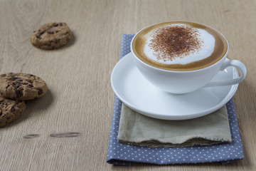 Tasse Cappuccino mit Kakao auf Holzplatte, Cookies  mit verschwommene  Hintergrund